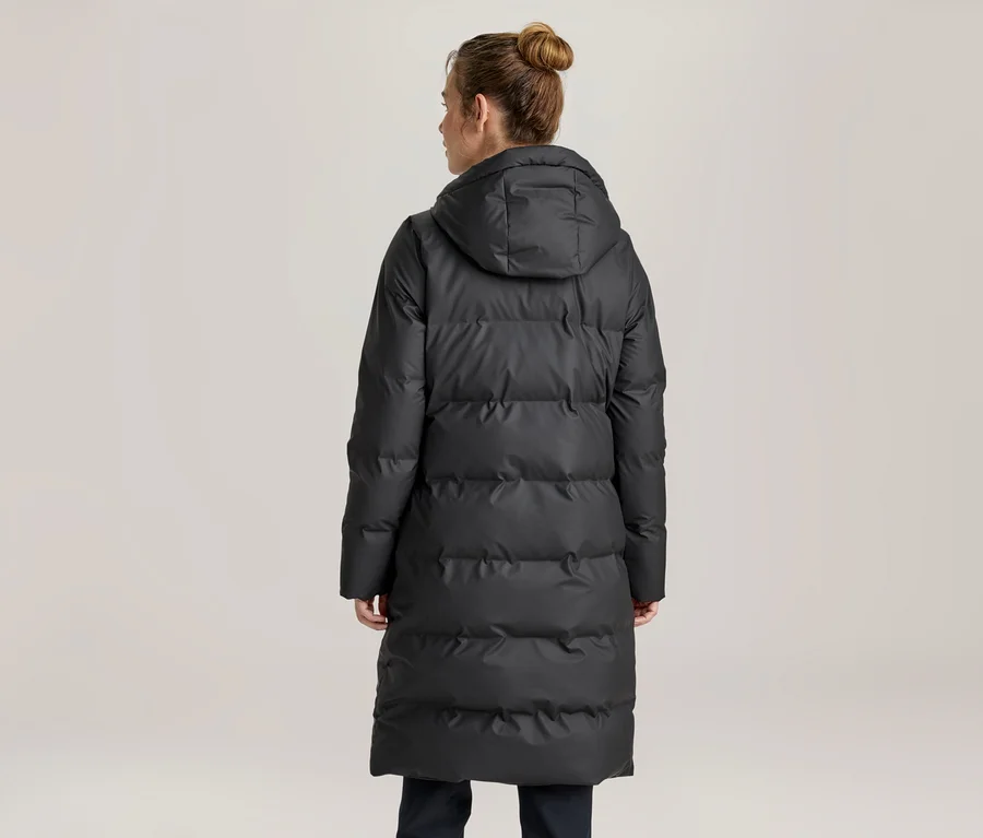 Femme vue de dos, portant un long manteau matelassé noir à capuche, les cheveux attachés en chignon.