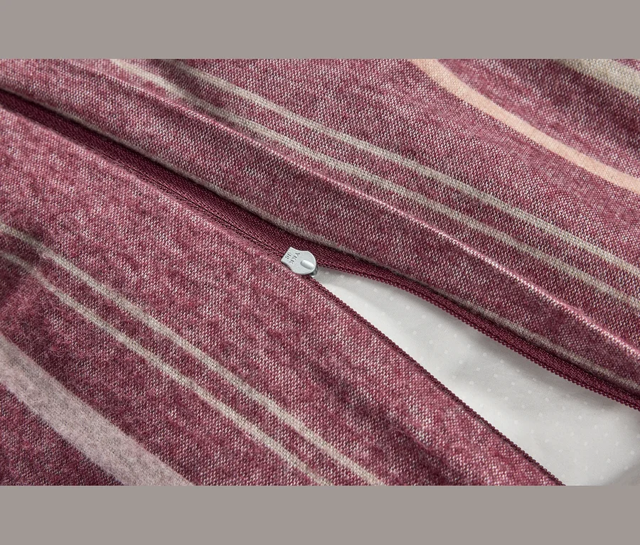 Gros plan d'un tissu rayé bordeaux et beige, probablement une housse de couette, avec une fermeture éclair partiellement ouverte révélant un tissu blanc en dessous.