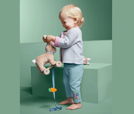 Un jeune enfant joue avec un lapin en peluche à roulettes et porte un pantalon de survêtement.