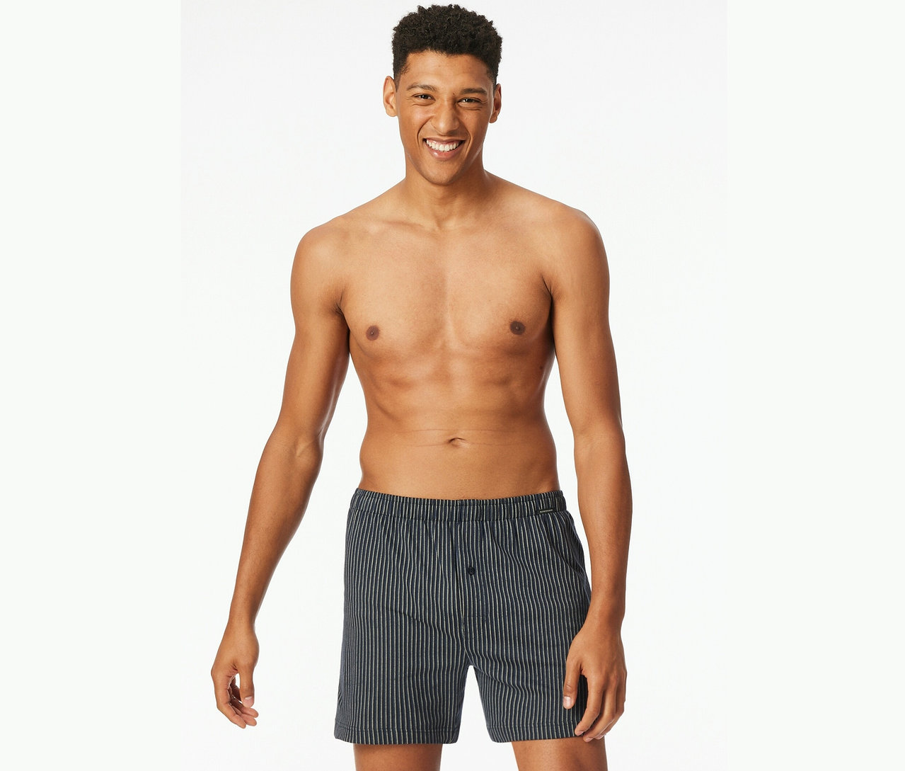 Un homme souriant, torse nu, porte un caleçon rayé.