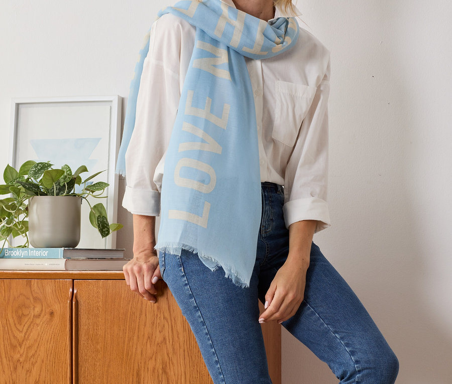 Femme blonde posant avec une écharpe tissée bleu clair avec l'inscription imprimée LOVE.
