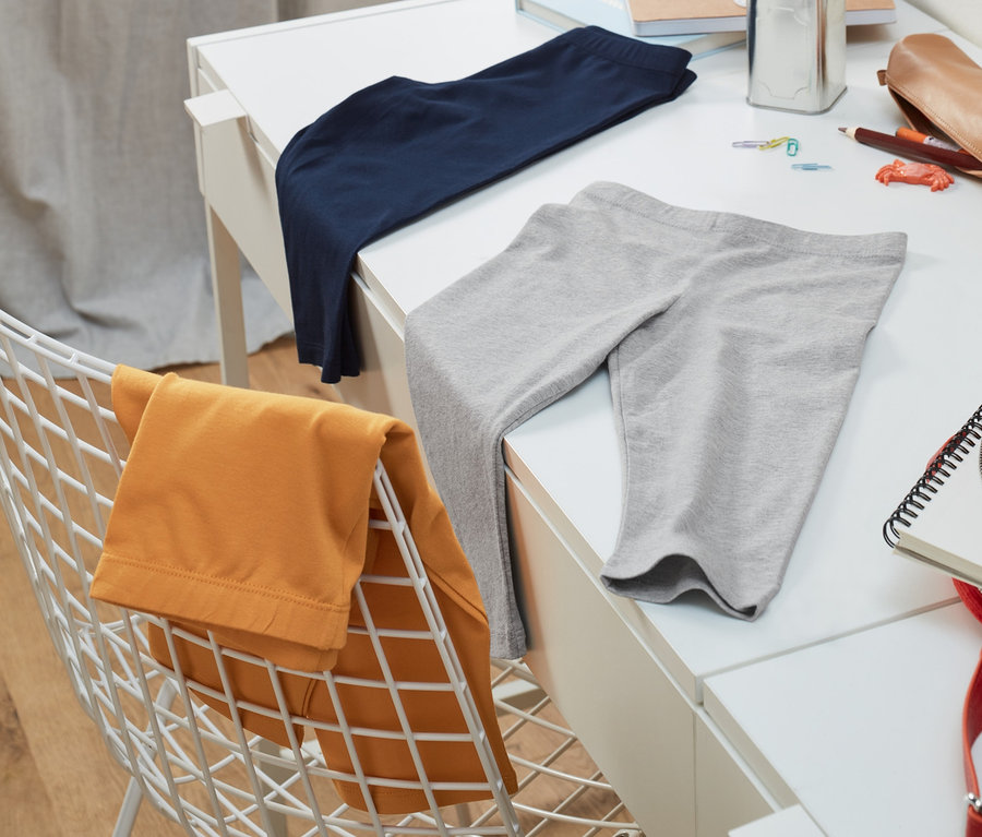 Trois leggings 3/4 gris, bleus et jaunes sont posés sur une table blanche. Les jaunes sont posés sur une chaise blanche.