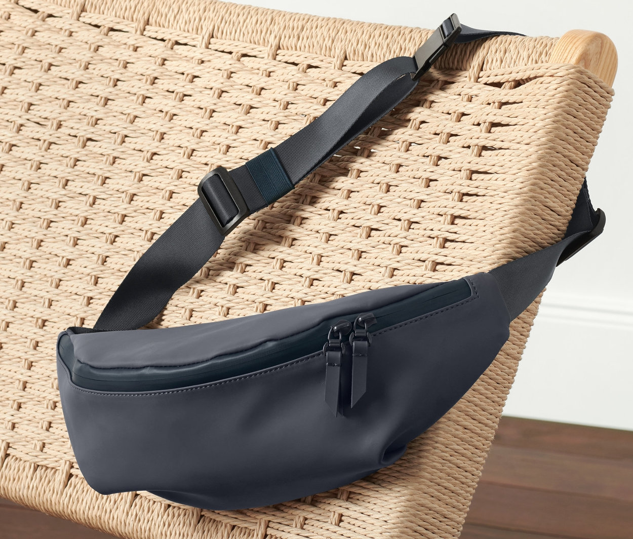 Un sac banane bleu marine repose sur un fauteuil en osier à côté de vêtements de sport roses.