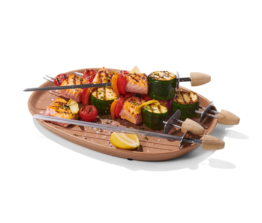 Quatre brochettes doubles avec saumon, courgettes, poivrons et tomates sur une assiette marron.