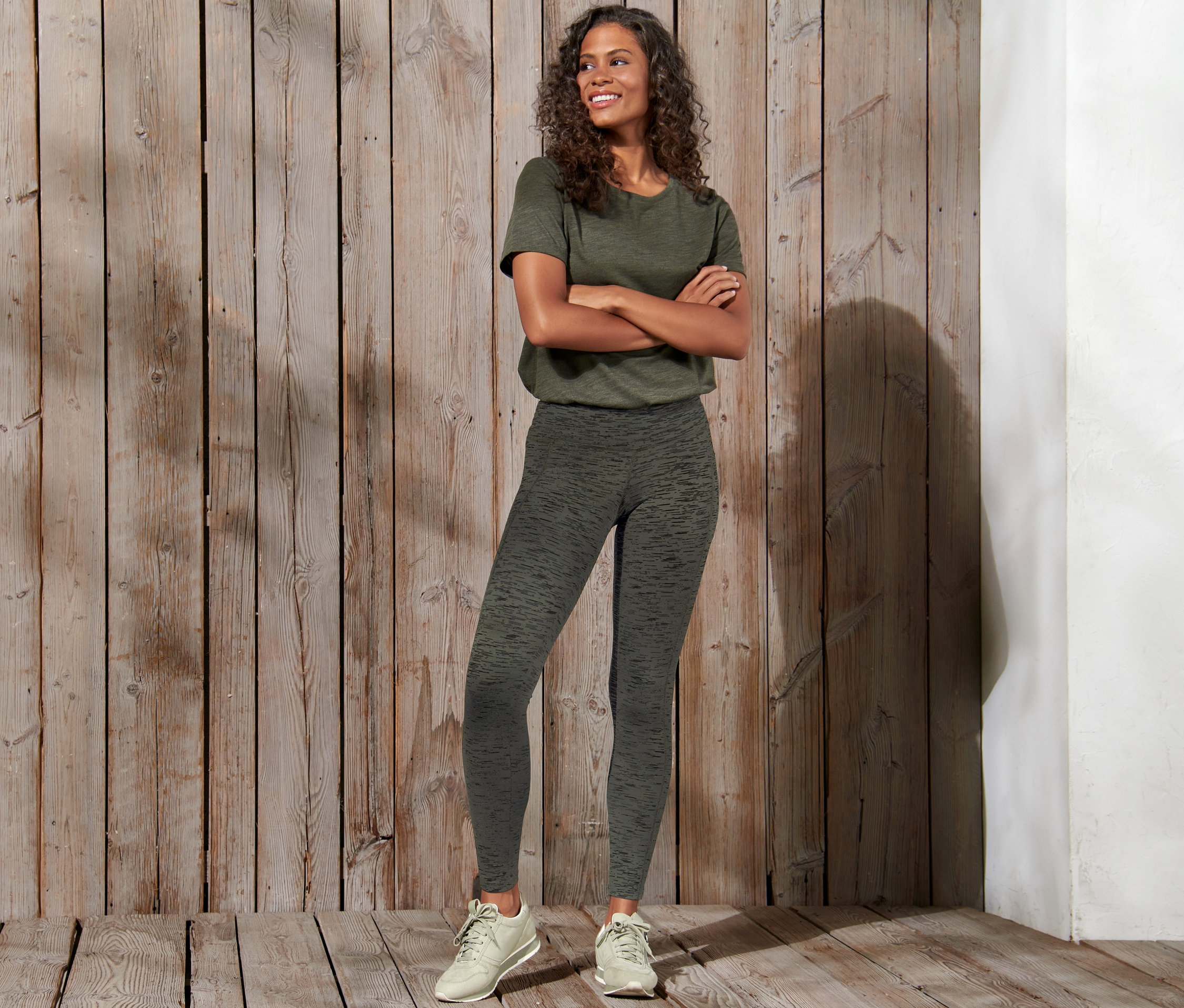 Une femme souriante pose, les bras croisés, et porte un legging de sport.