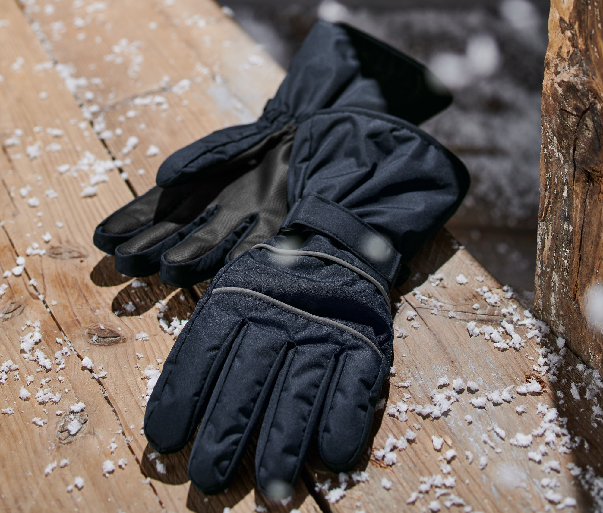 Des gants d'hiver bleu foncé sont posés sur une surface en bois saupoudrée de neige.