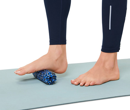 Pied sur mini-rouleau pour fascias sur un tapis de gymnastique.