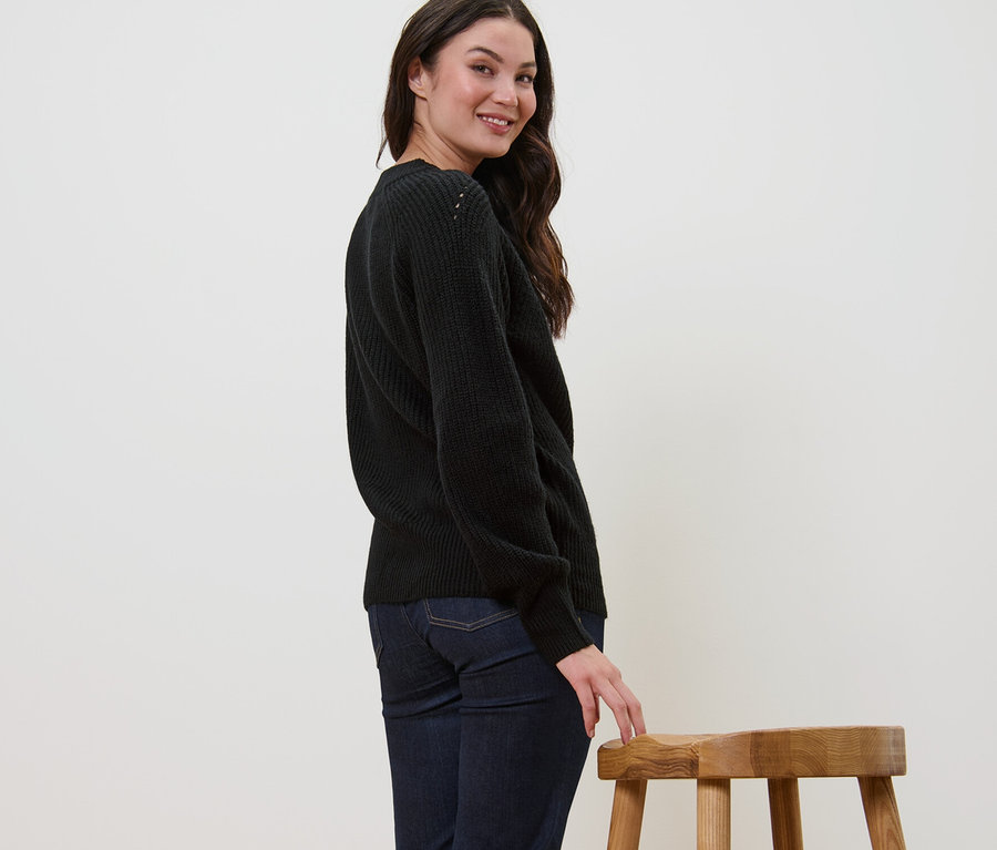 Femme souriant par-dessus son épaule et posant en pull en maille noir.