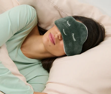 Une femme dort avec un masque de nuit sur les yeux.