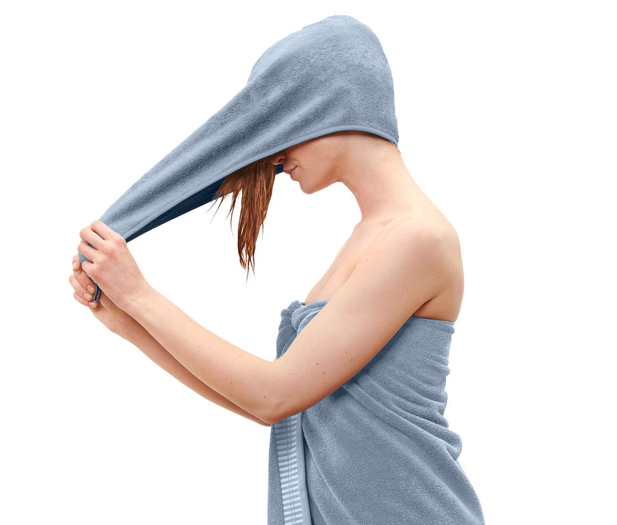 Une femme met une serviette turban bleu clair sur sa tête.