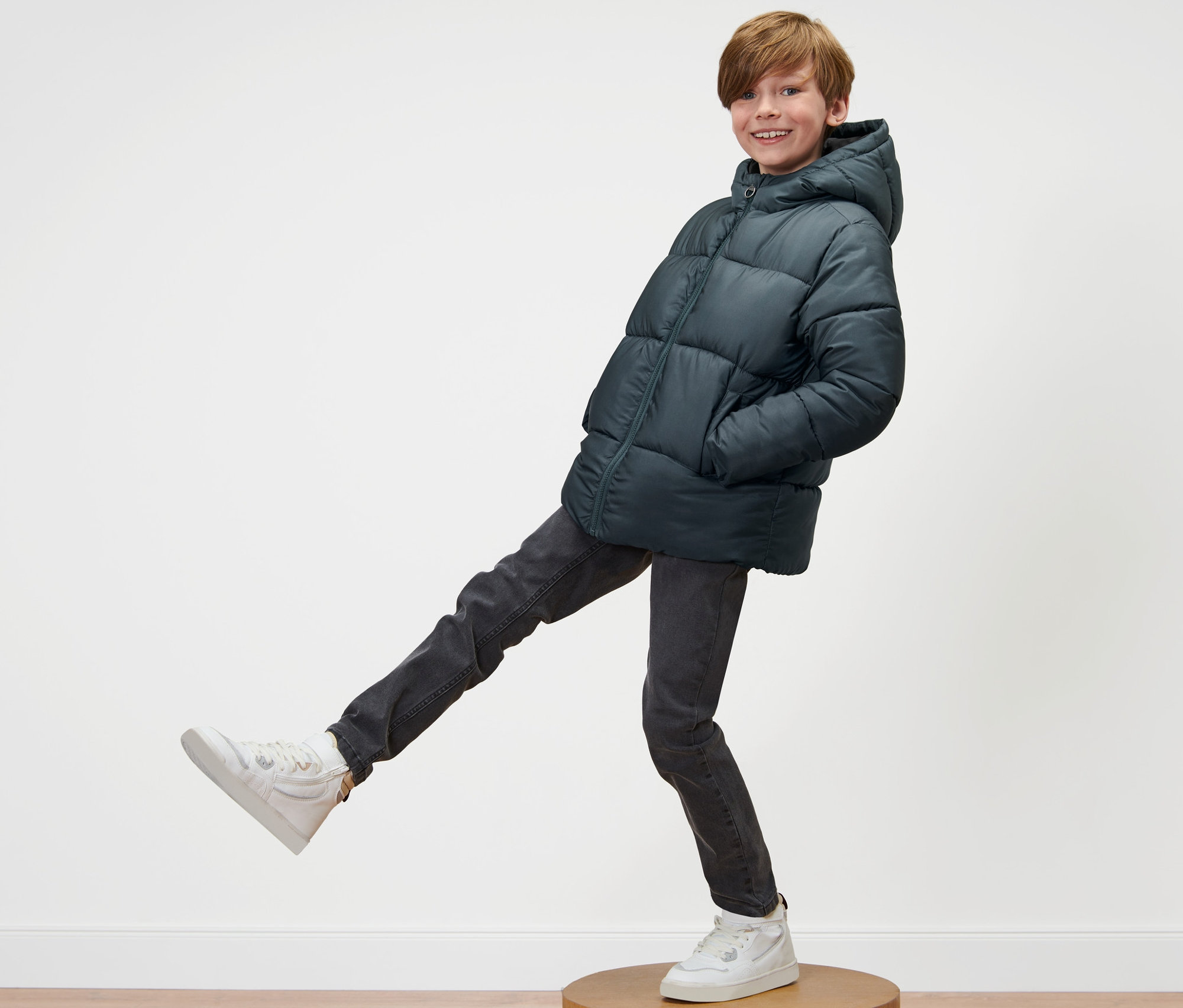 Garçon posant sur un socle en bois en veste thermique enfant et baskets.