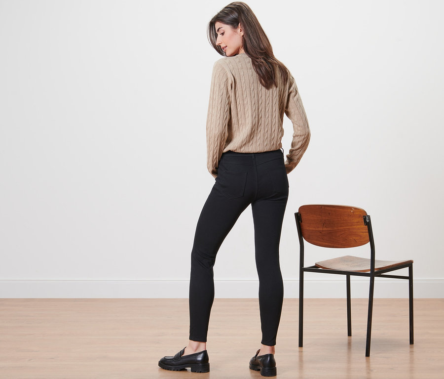 Une femme se tient dos à la caméra et porte un pull beige et un jegging.