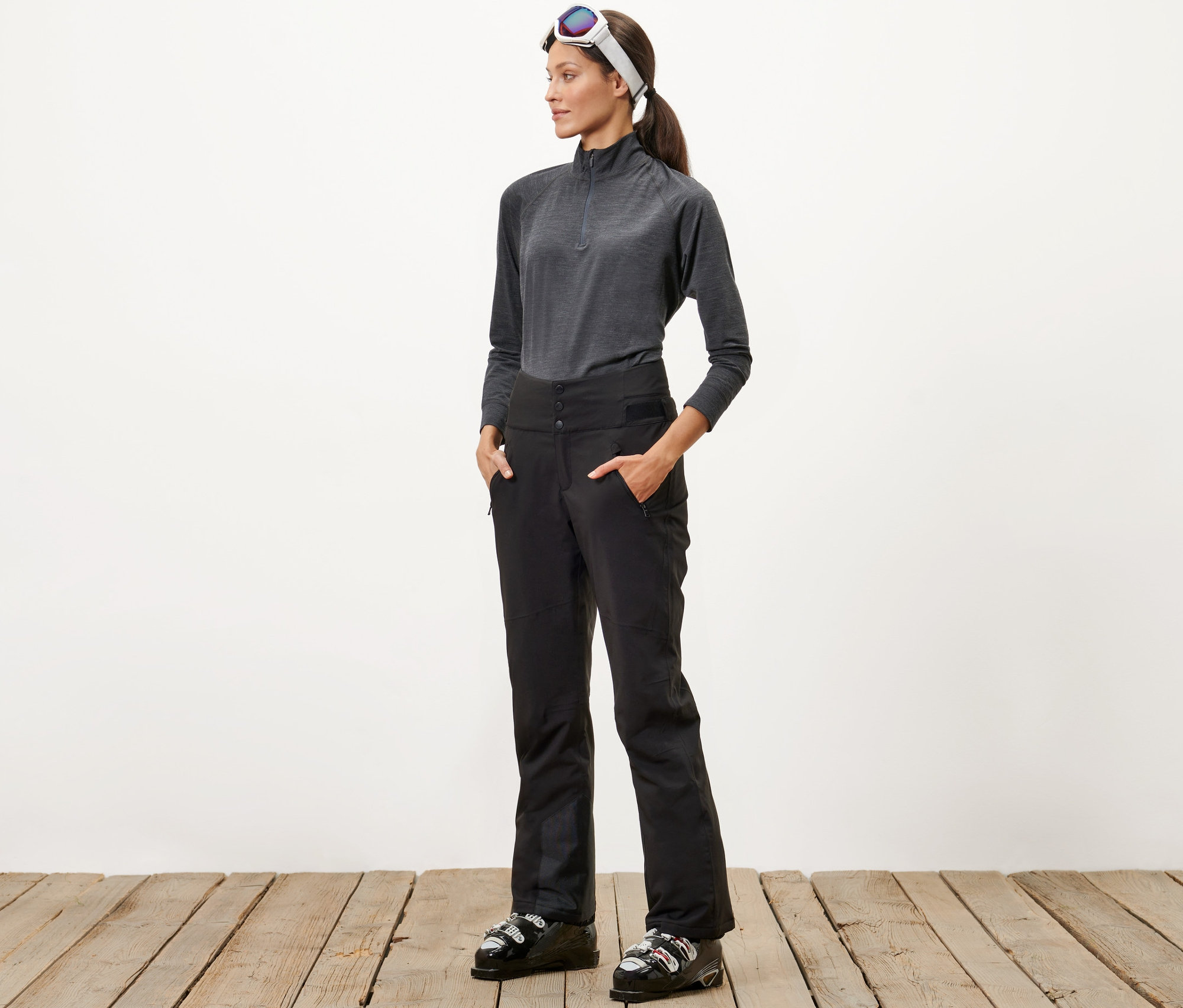 Une femme se tient debout, les mains dans les poches de son pantalon de ski taille haute.