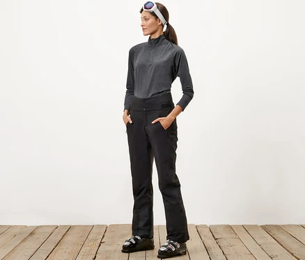 Une femme se tient debout, les mains dans les poches de son pantalon de ski taille haute.