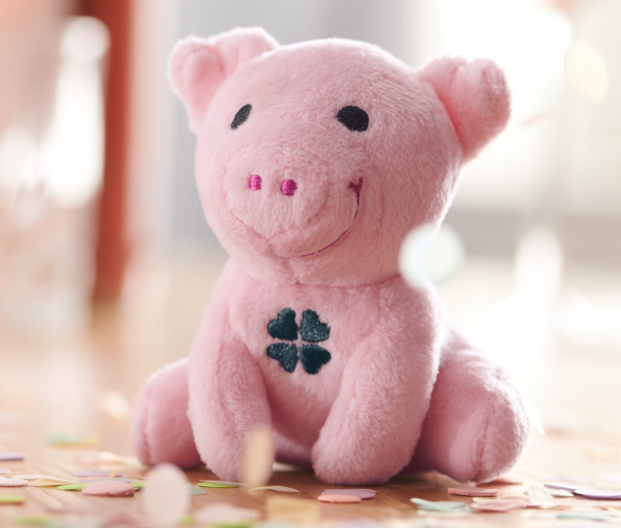 Un cochon porte-bonheur sonore rose assis avec un trèfle sur le ventre, entouré de confettis.