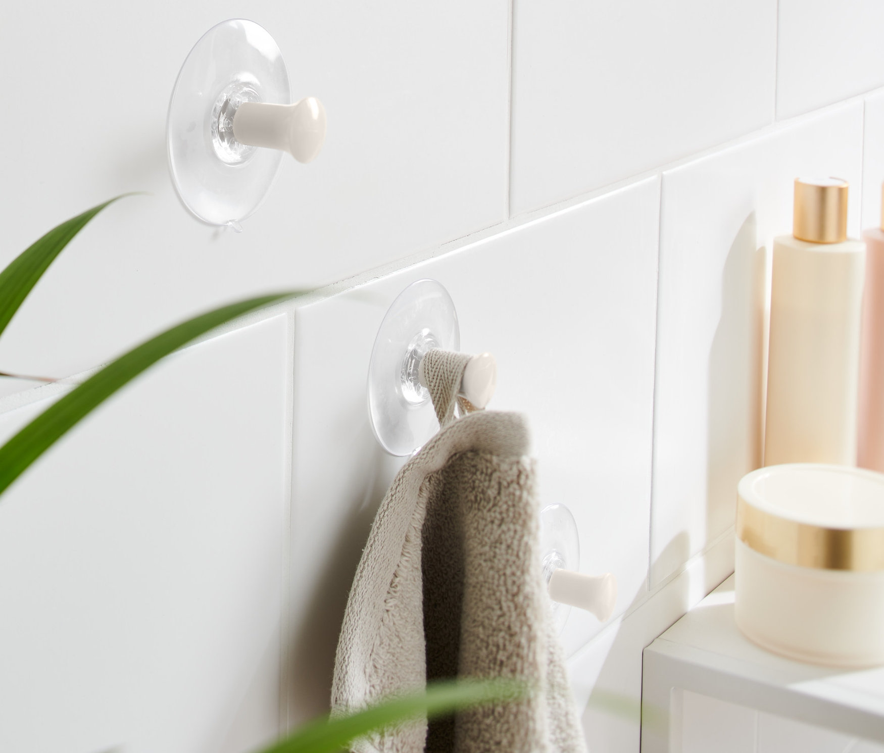 Deux 3 crochets à ventouse sont fixés sur des carreaux blancs, une serviette est suspendue à l'un d'eux.
