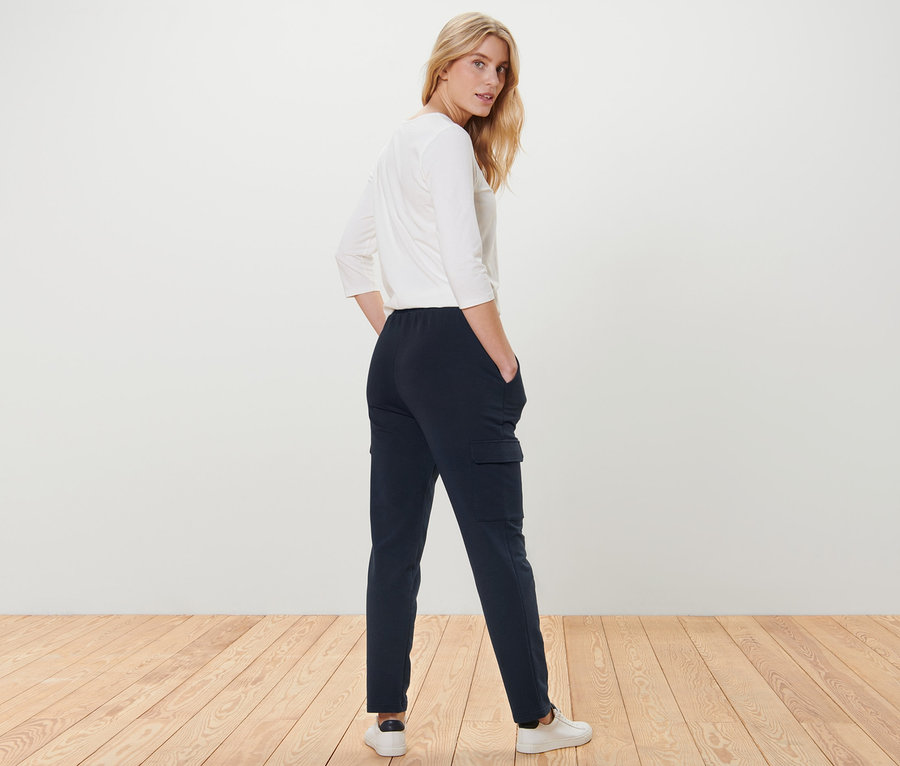 Une femme pose en pantalon de jogging cargo bleu foncé et haut blanc.