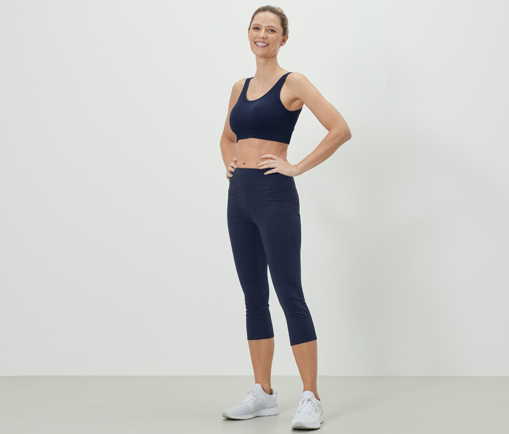 Femme posant en soutien-gorge de sport bleu foncé et collant de sport 3/4.