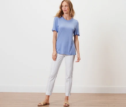 Une femme debout portant une chemise bleu clair avec des fronces et un pantalon blanc.