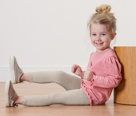 Fillette souriante assise par terre avec des leggings unis pour enfant.