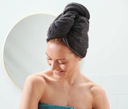 Femme avec une serviette turban anthracite sur la tête et une serviette bleue enroulée autour du corps.
