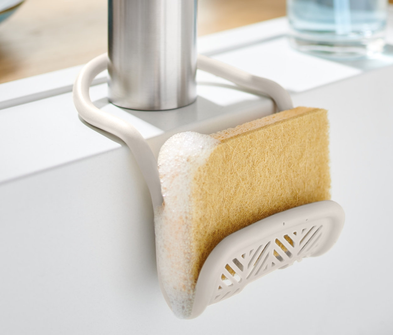Porte-éponge avec éponge fixé à un robinet dans un évier blanc.