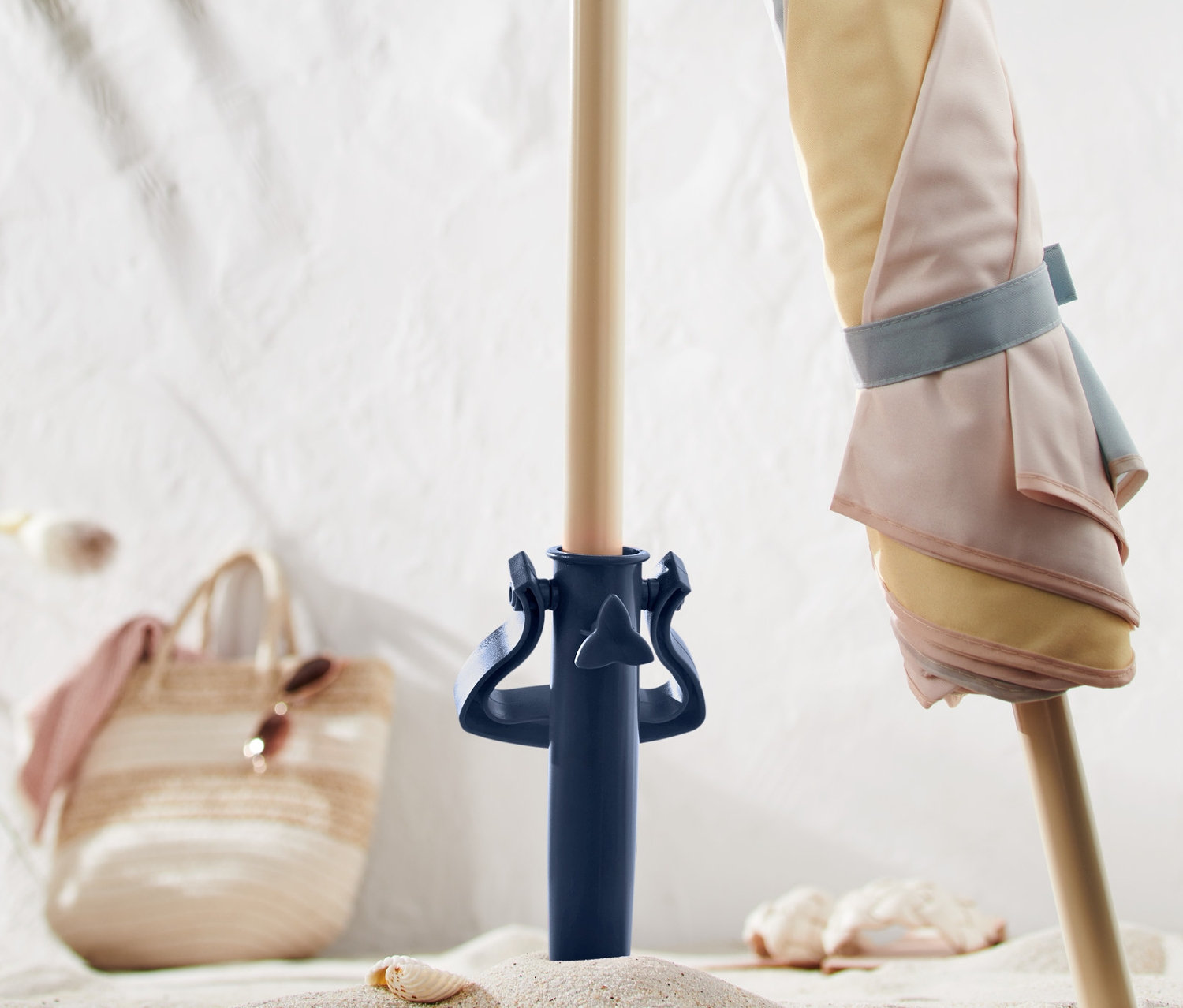 Un parasol à rayures pastel est fixé dans un support à parasol à vis bleu dans le sable.
