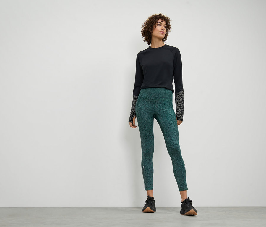 Une femme debout porte un legging de sport et un haut noir à manches longues.