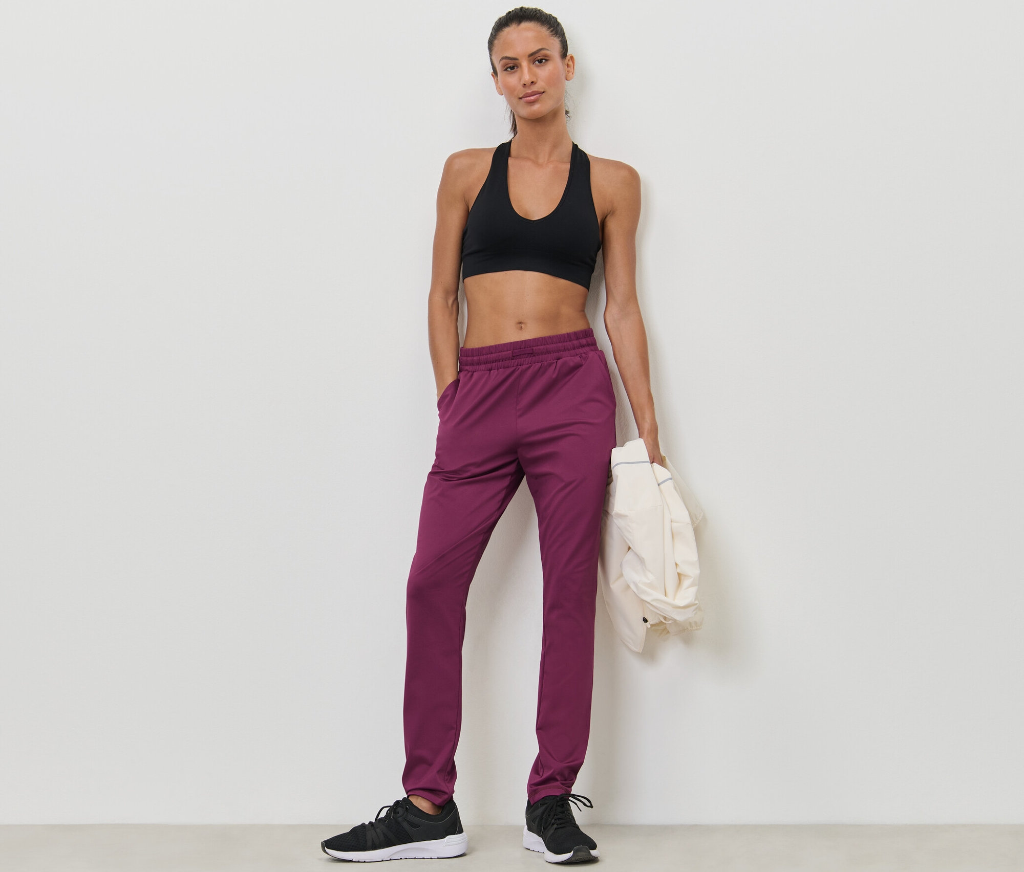Une femme pose en soutien-gorge de sport et pantalon de sport rouge baie.
