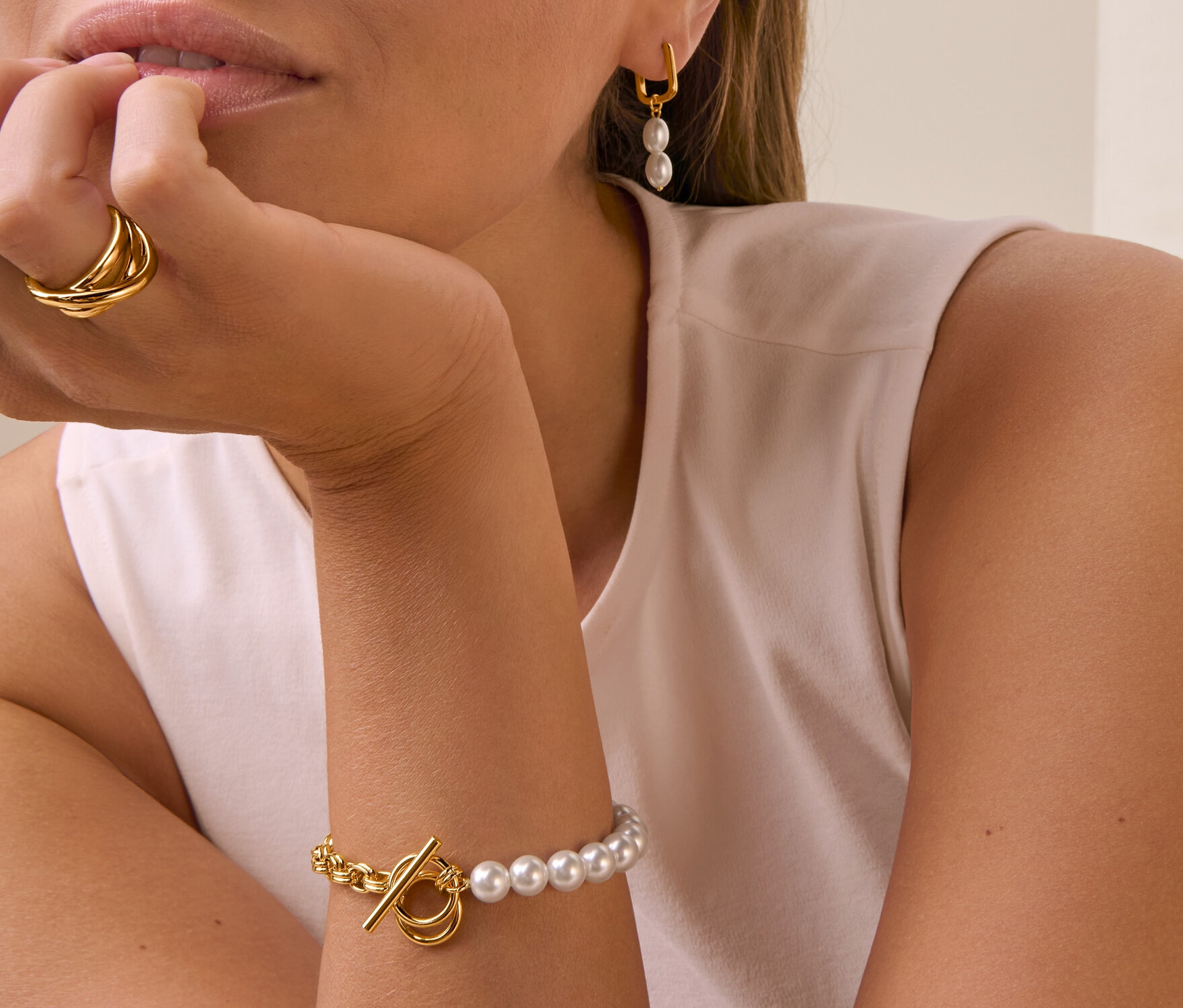 Femme portant des Boucles d’oreilles pendantes avec perles, une Bague Loops et un Bracelet moitié perle.