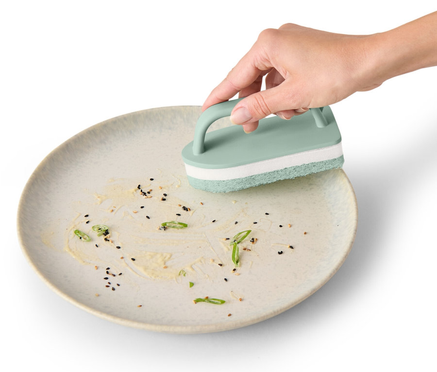 Une main nettoie une assiette avec l'outil de nettoyage pour carrelage.