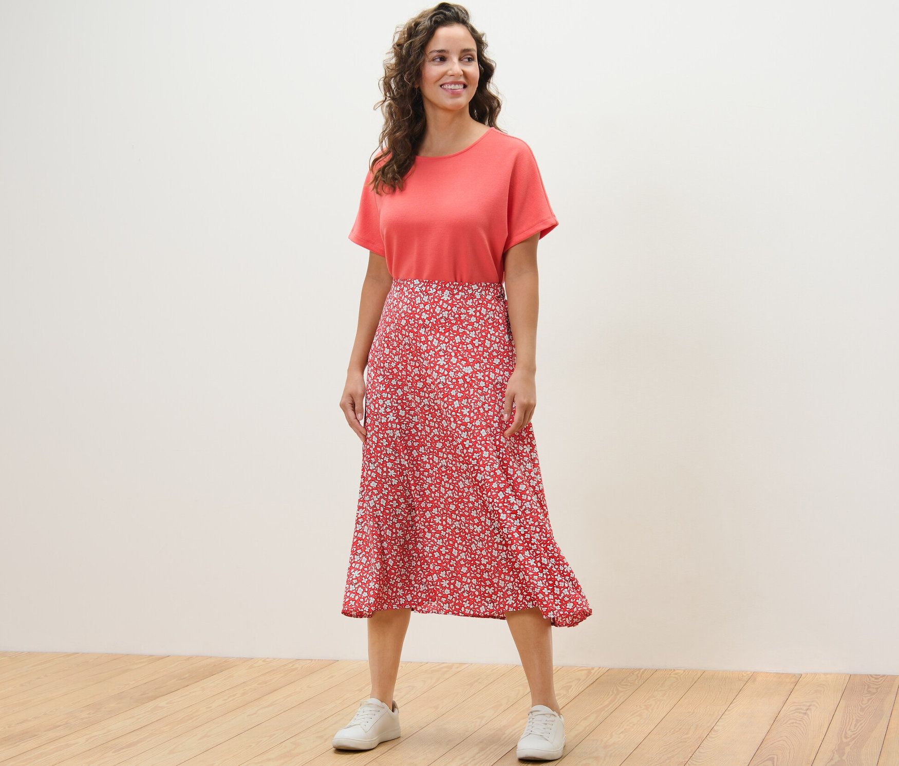Une femme debout sur un plancher en bois porte une jupe midi imprimée corail.
