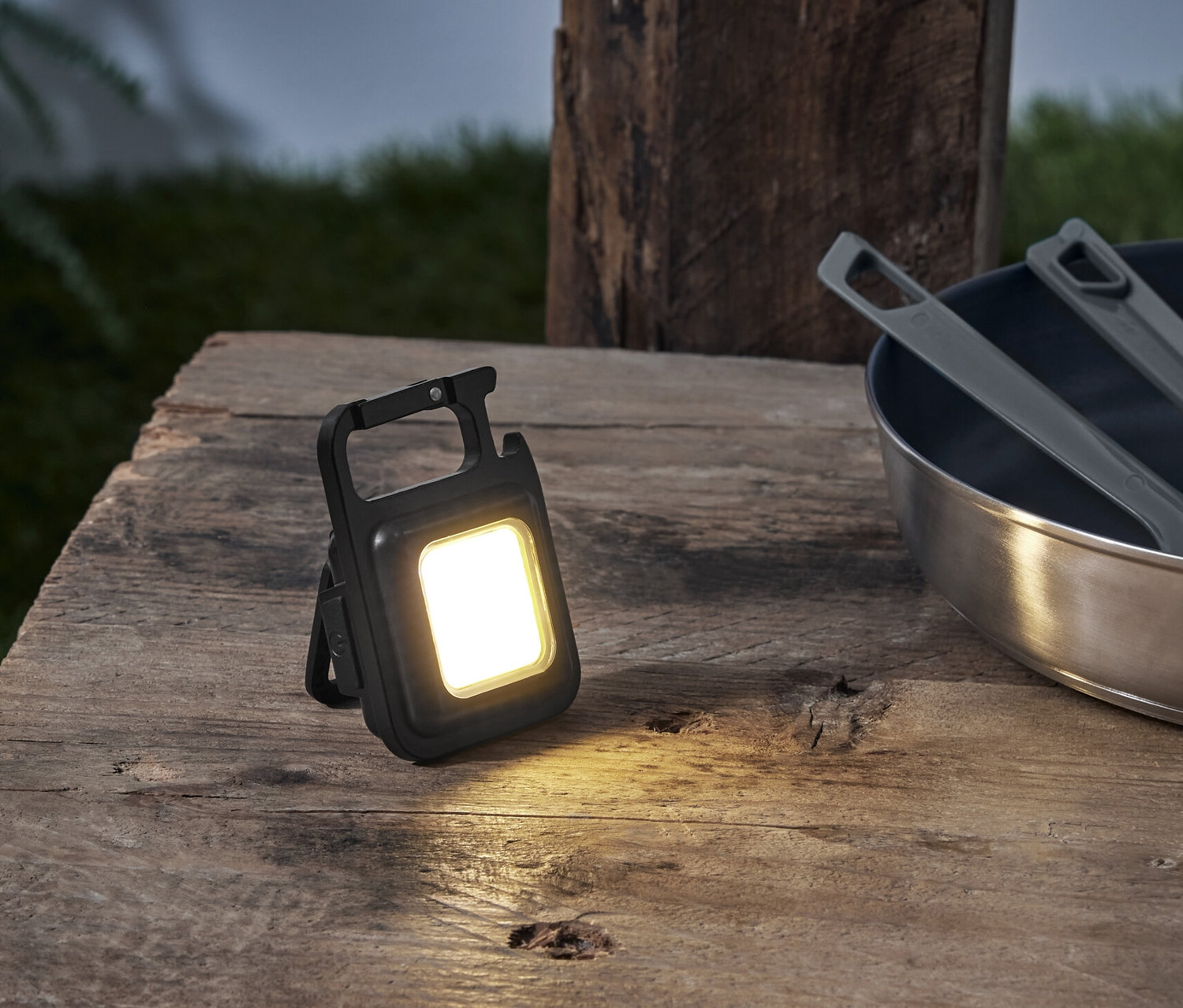 Sur une table en bois se trouvent une lumière multifonction, une poêle et un sac à dos.