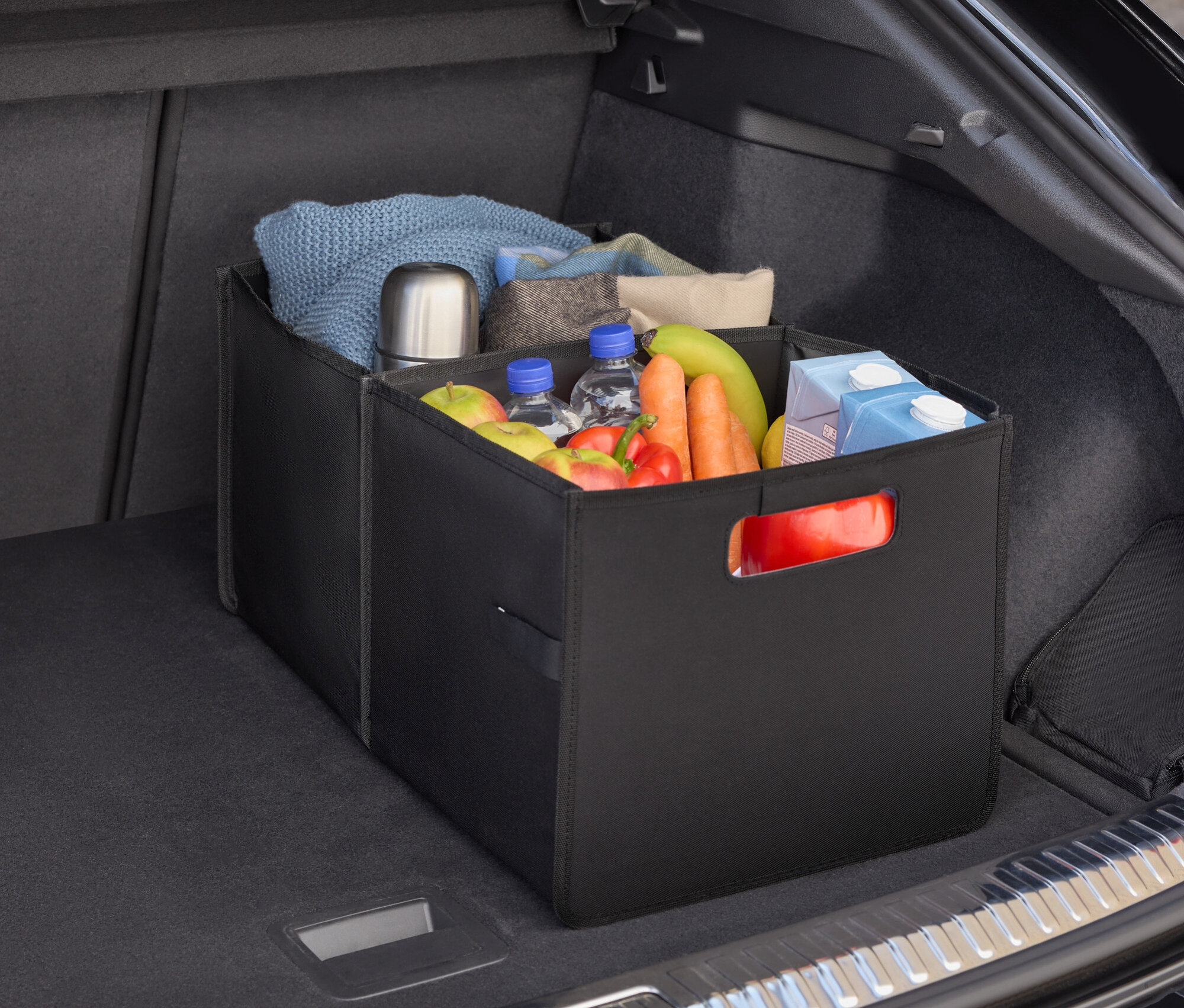 Dans le coffre d'une voiture, un organisateur noir rempli de nourriture, de bouteilles d'eau, de fruits et de légumes.