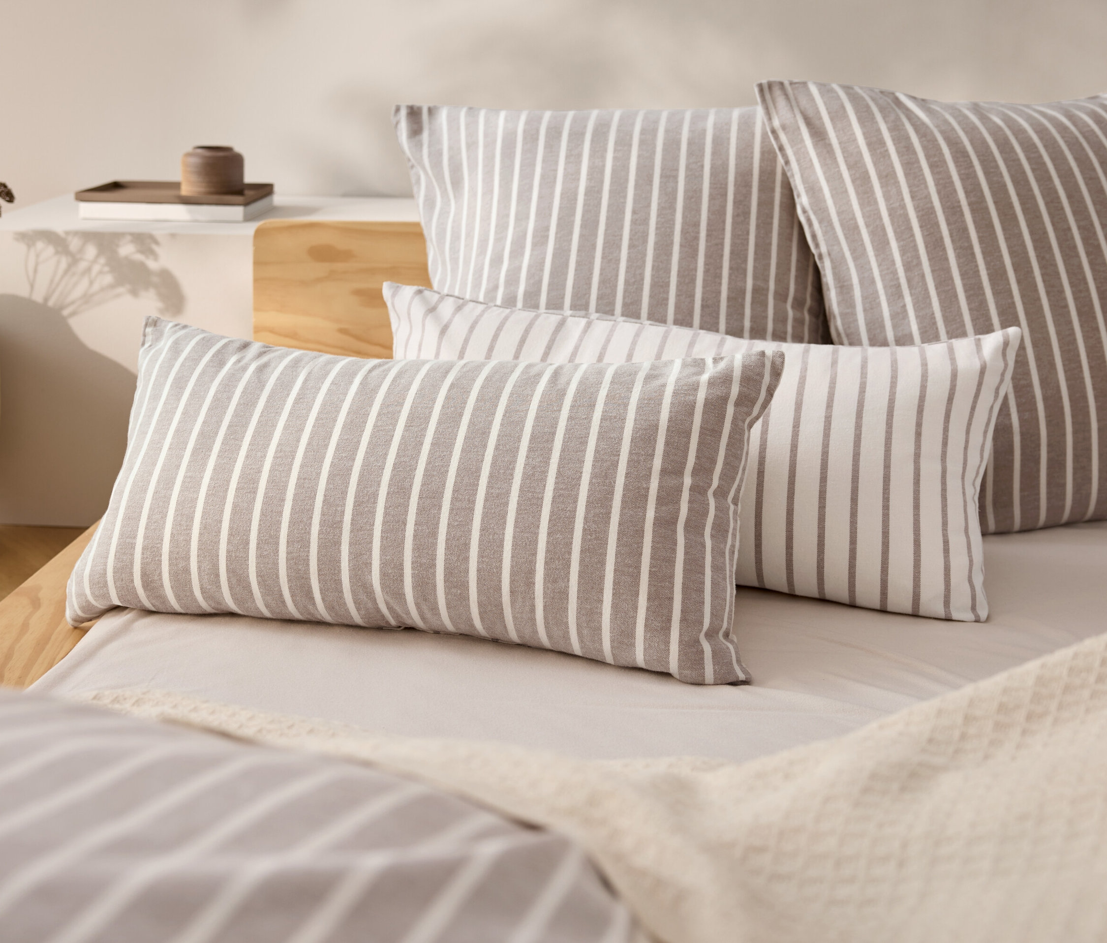Quatre coussins rayés sur un lit avec un couvre-lit beige.