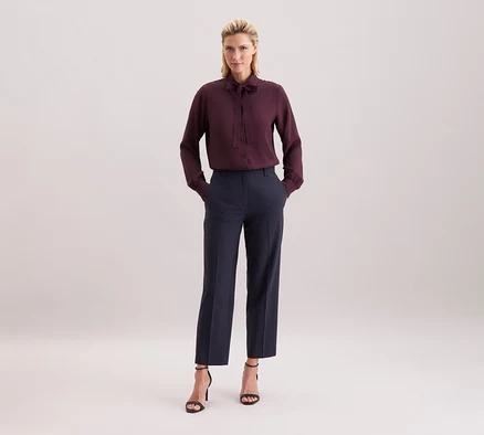 Femme portant un chemisier à col lavallière en viscose Seidensticker bordeaux, un pantalon foncé et des sandales noires.
