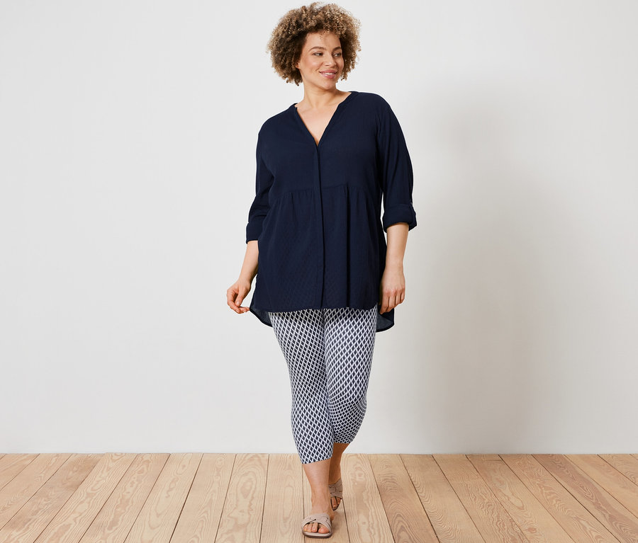 Une femme porte une blouse longue et un legging 3/4 imprimé.