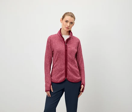 Une femme porte une veste polaire à manches longues avec fermeture éclair et un pantalon bleu foncé.