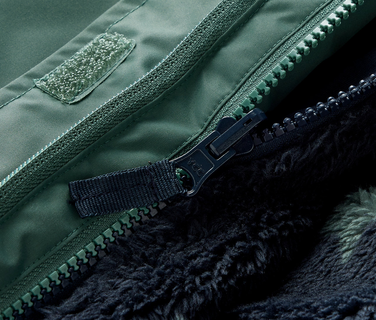 Gros plan sur la fermeture éclair et le velcro d'une veste d'hiver verte 3 en 1 pour enfants.