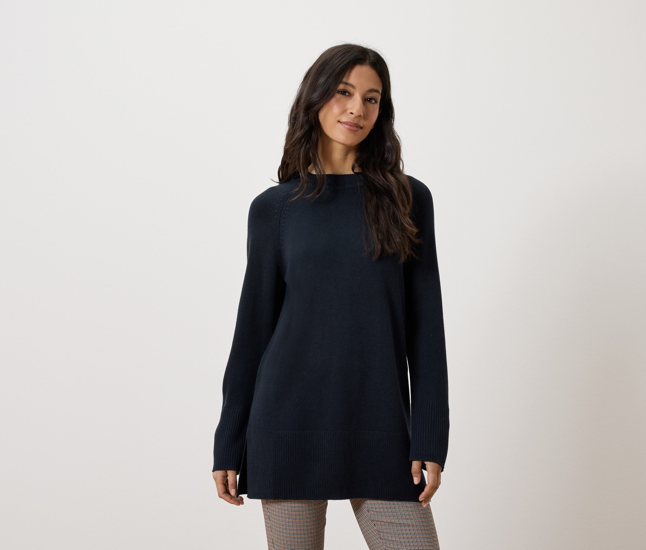 Une femme porte un long pull bleu foncé et un pantalon marron.