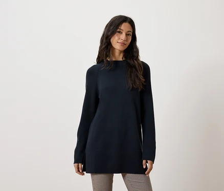 Une femme porte un long pull bleu foncé et un pantalon marron.