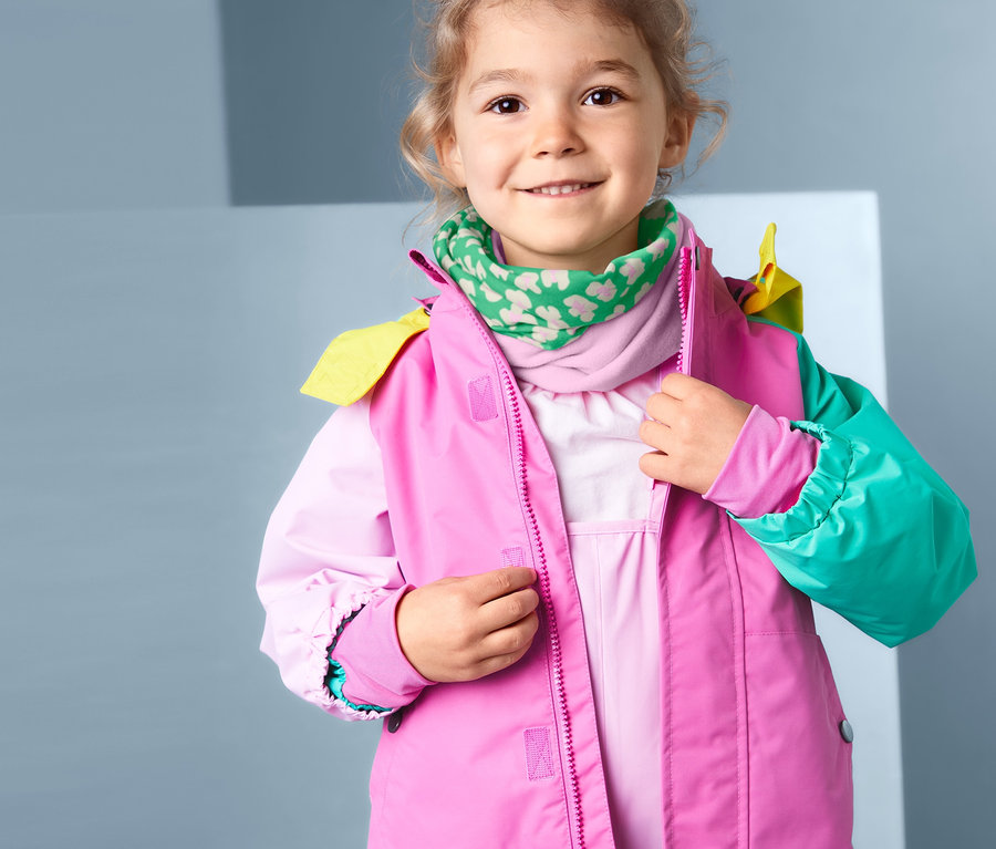 Une fille ferme une veste rose et porte un foulard multifonction recyclé, rose et vert.