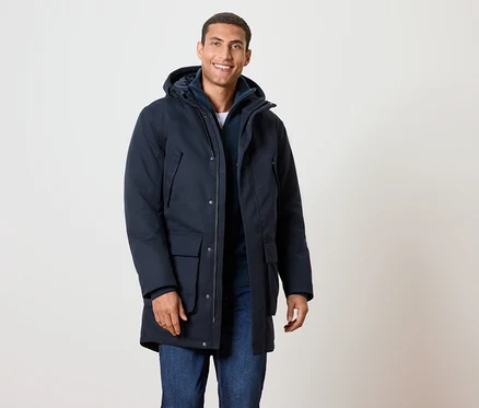 Un homme souriant portant une veste d'hiver bleu marine à capuche et un jean.