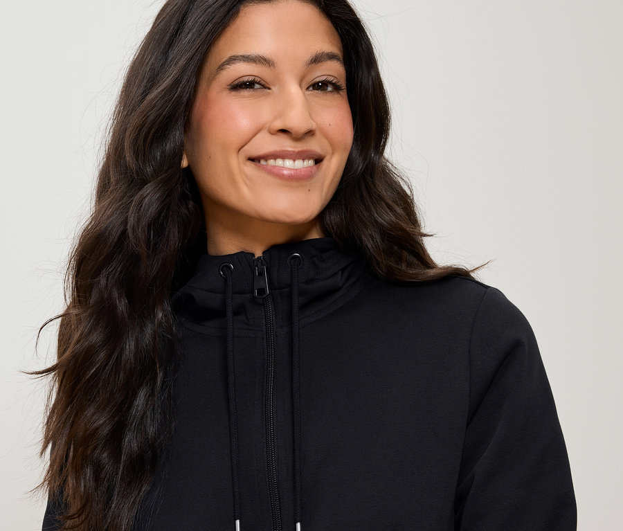 Portrait d'une femme aux longs cheveux bruns portant un sweat à capuche noir zippé.