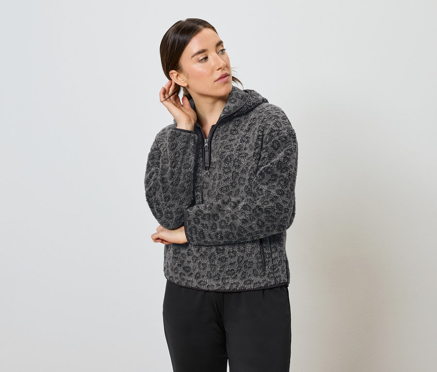 Femme posant dans un sweat à capuche en polaire léopard gris et noir et un pantalon noir.