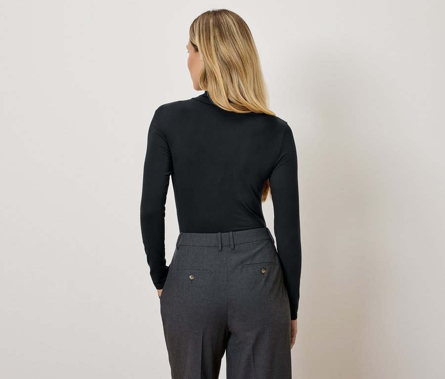 Vue arrière d'une femme blonde portant un pull à col roulé noir et un pantalon gris.