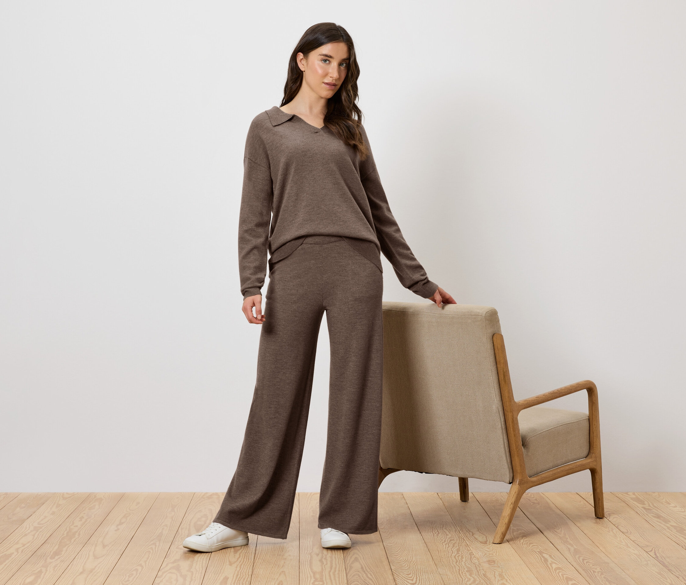 Femme en ensemble tricoté marron posant à côté d'un fauteuil.