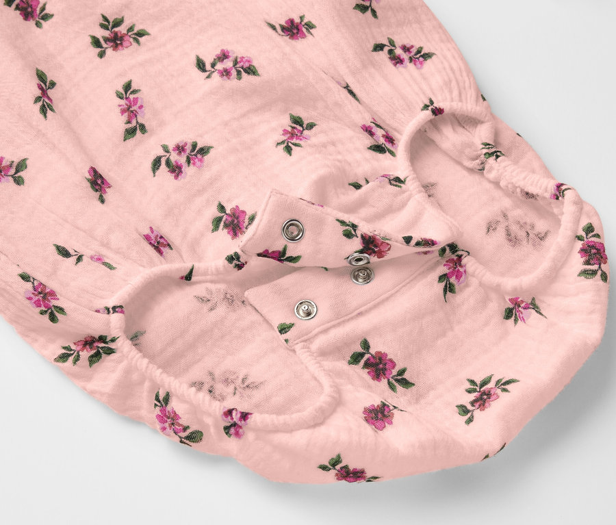 Gros plan sur un body en mousseline pour bébé avec un motif floral et une fermeture à boutons-pression.
