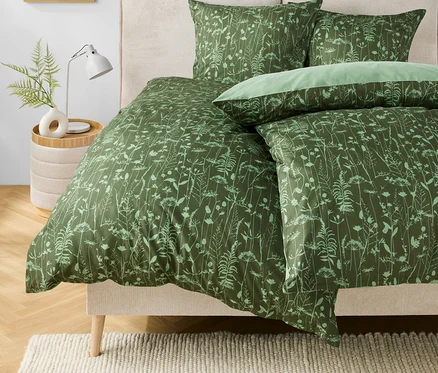 Linge de lit vert à motifs floraux sur un lit. Une lampe et un vase avec une plante sont posés sur la table de chevet.