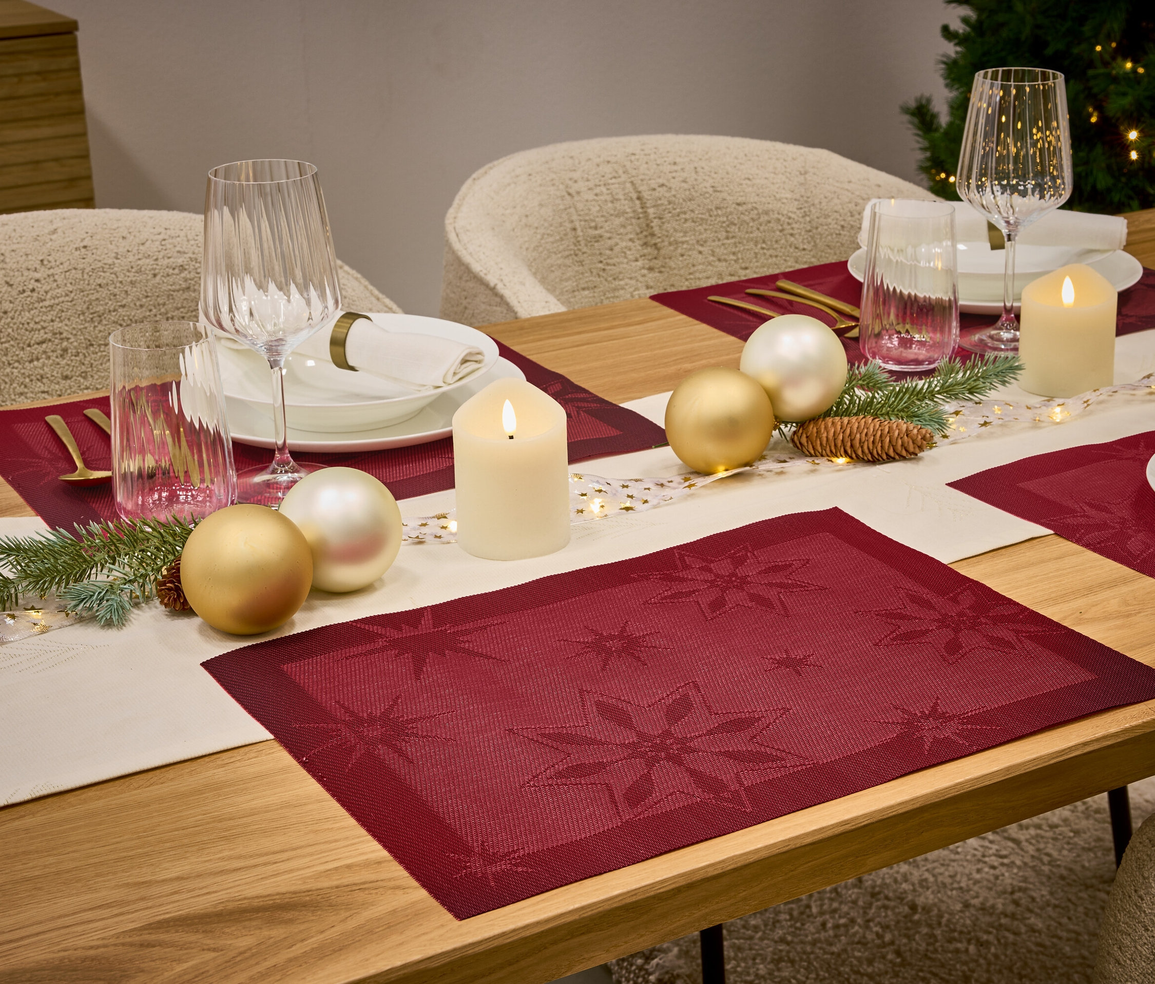 Une table dressée avec des sets de table rouges, un chemin de table blanc, des bougies, des verres et des décorations de Noël.
